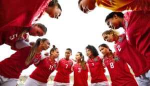 Teammates in red uniforms huddle in a circle.