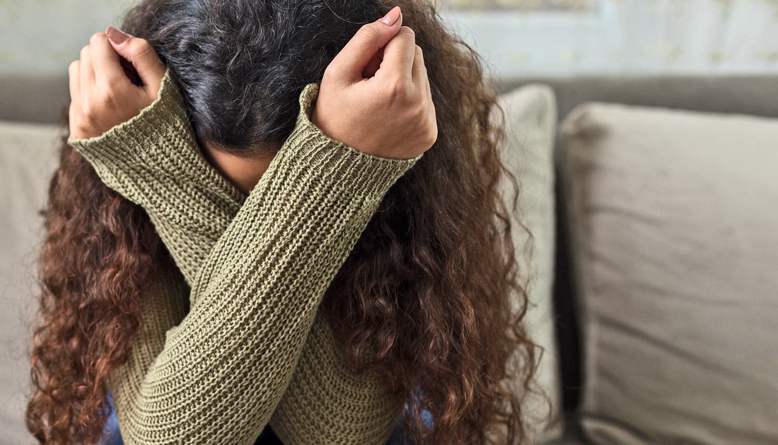 A young woman covers her face with her arms.