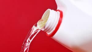 Bleach pours from a white bottle against a red background.