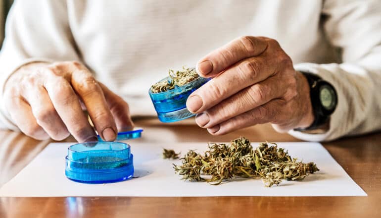A person grinds up cannabis while sitting at a table.