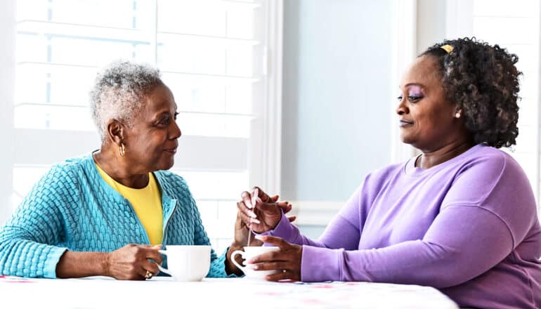 A mother and daughter sit together at a kitchen table drinking tea.