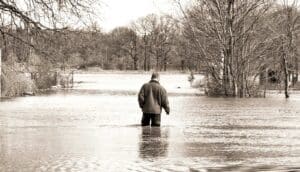 A man stands in flood water on a rural property.