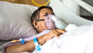 A patient lies in a hospital bed with a breathing mask on.