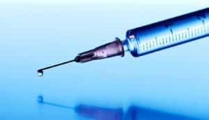 A syringe with a droplet of vaccine coming from the needle.