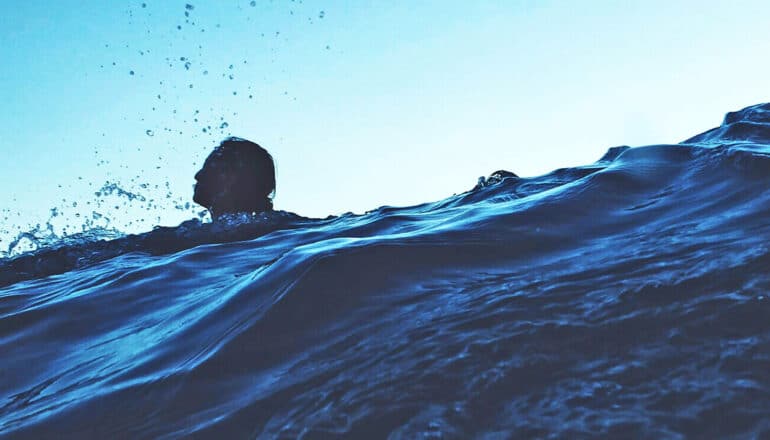 A person swims in the ocean with only his head poking above the water.
