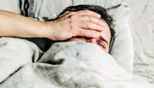 A man laying in bed puts his hand over his face.