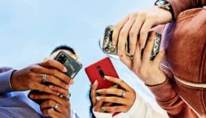 Three people look at their phones with the camera below them looking up.