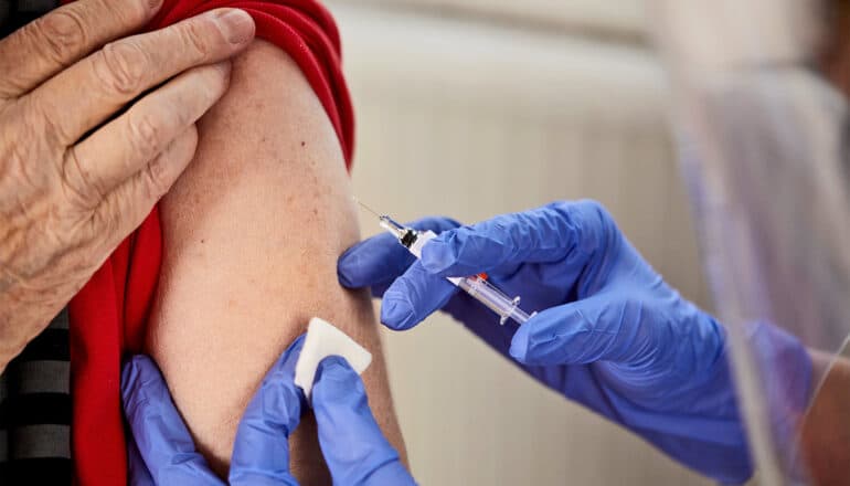 A health worker with blue gloves is giving a person a Covid vaccine.