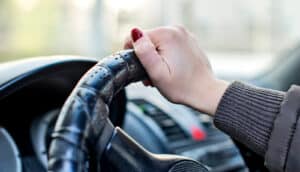 A woman with red nails has her hand on a car's steering wheel.