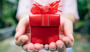 A person holds a small red box with a ribbon on its lid.