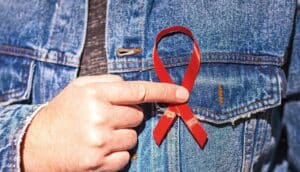 A person holds a red ribbon to their chest.