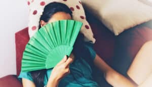 A woman lays on a couch while using a green fan.