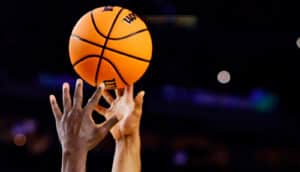 Two players reach for a midair basketball.