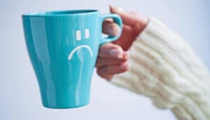 A person holds a coffee mug with a frowning face on it.