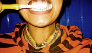 A person in an orange and black striped hoodie brushes their teeth.