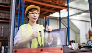 A forklift operator works in a factory while wearing safety gear.