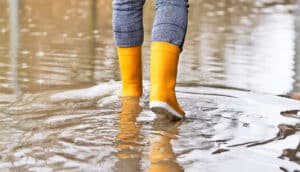 A person walks through a flooded street wearing yellow rainboots.