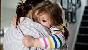 A little girl hugs onto her mother and grips her shirt.