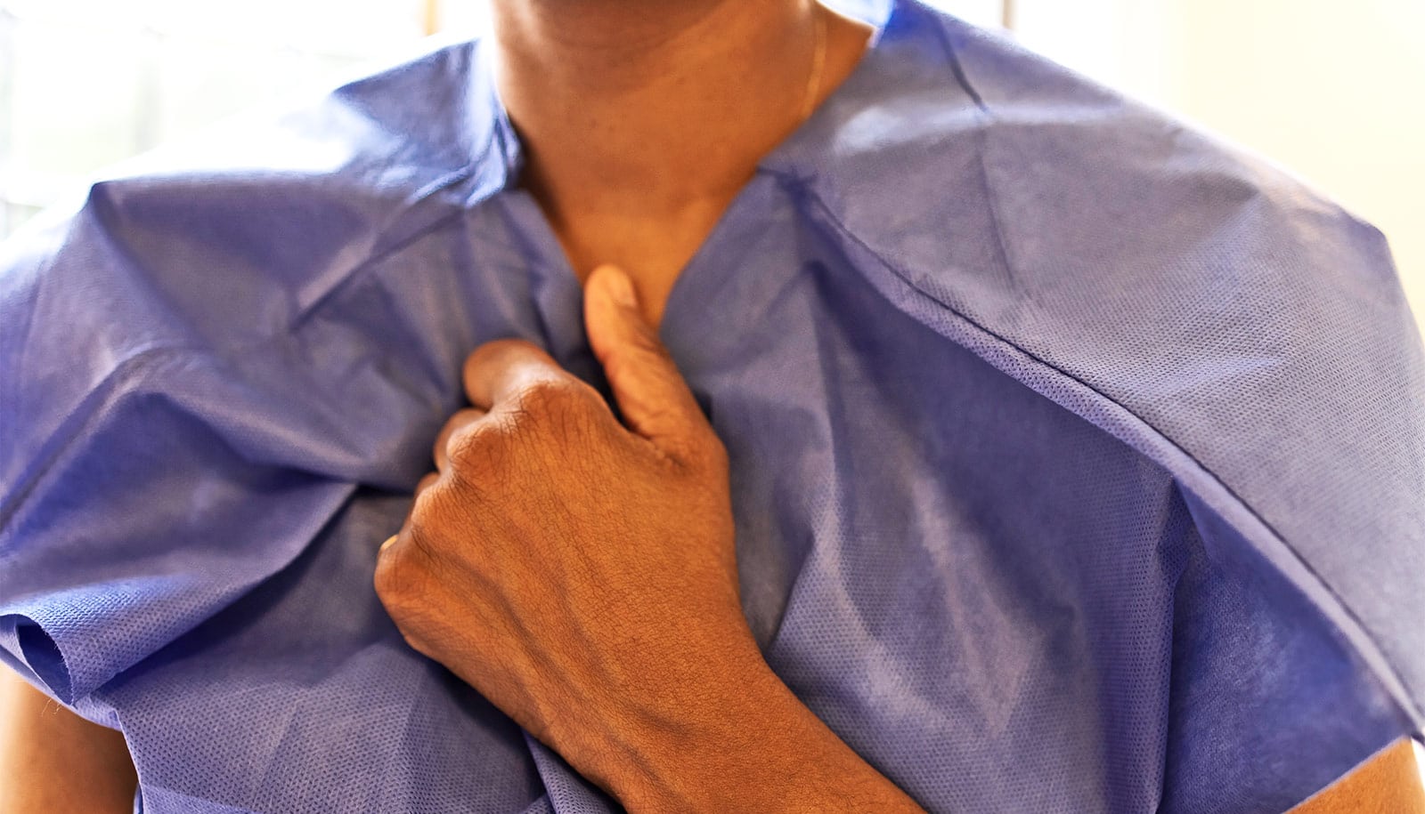 A woman holds her hand to her chest nervously while wearing a medical gown.
