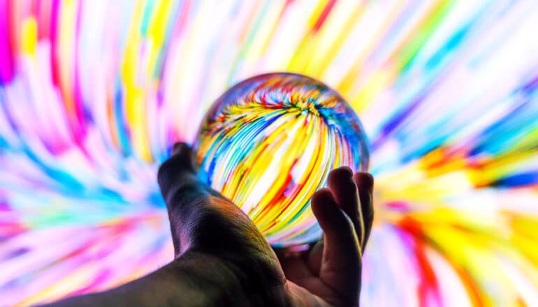 A person holds a glass ball that's refracting colorful beams of light from behind it.