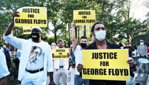 Protestors hold signs that read "Justice for George Floyd" while gathered at a park.