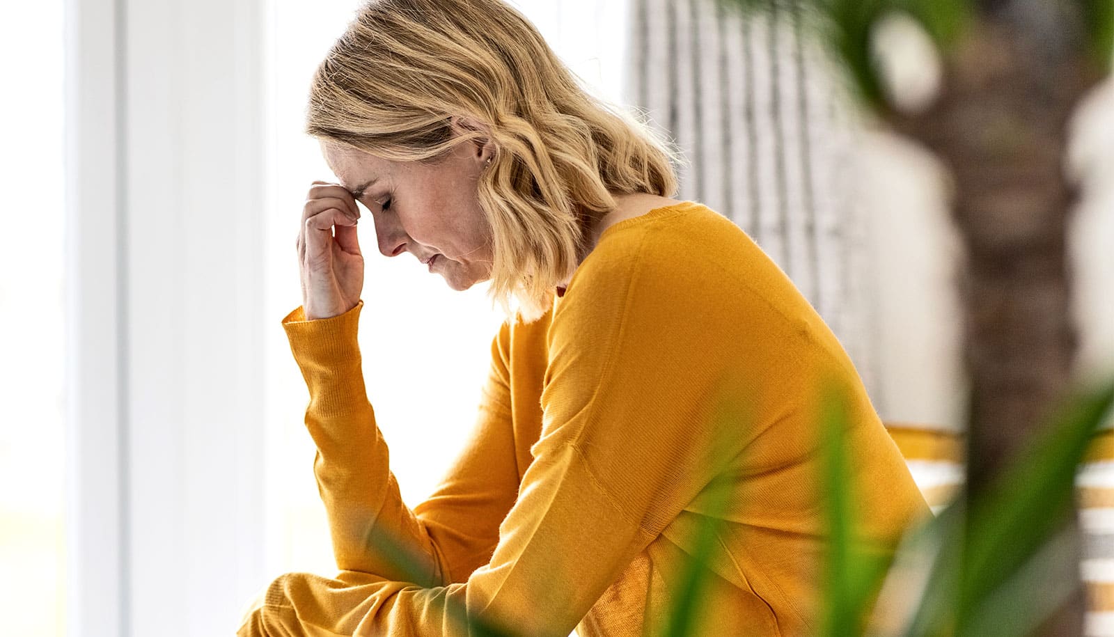 A woman holds the bridge of her nose in pain and closes her eyes.