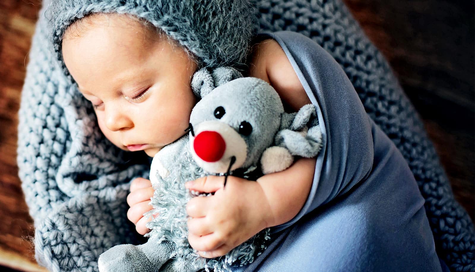 A baby sleeps with a mouse stuffed animal toy.