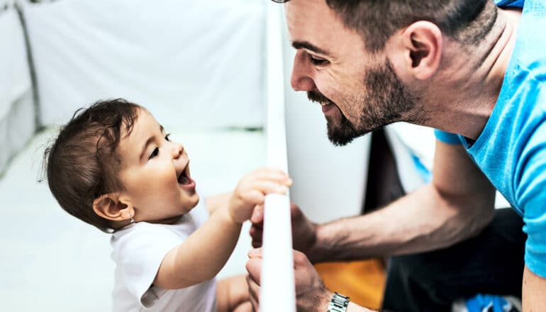 A father leans over his child's crib and talks to the baby.