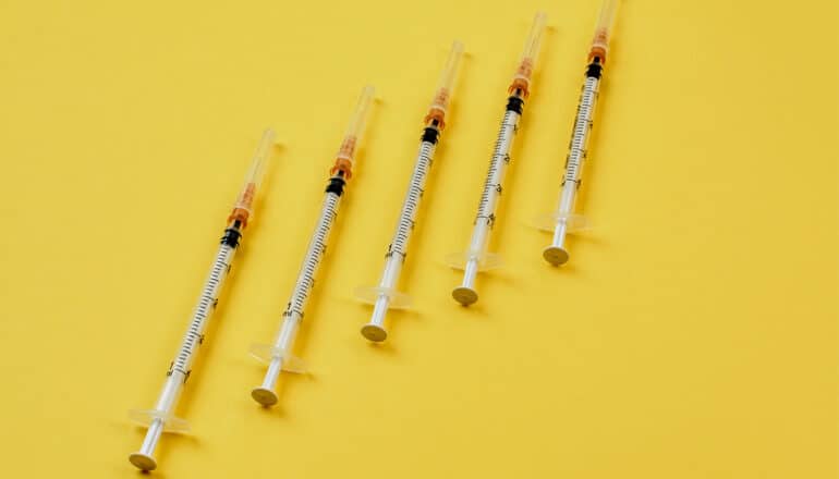 A row of insulin syringes on a yellow background.