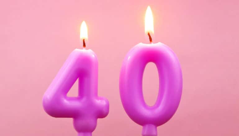 Birthday candles in the shape of the number 40 burn against a pink background.
