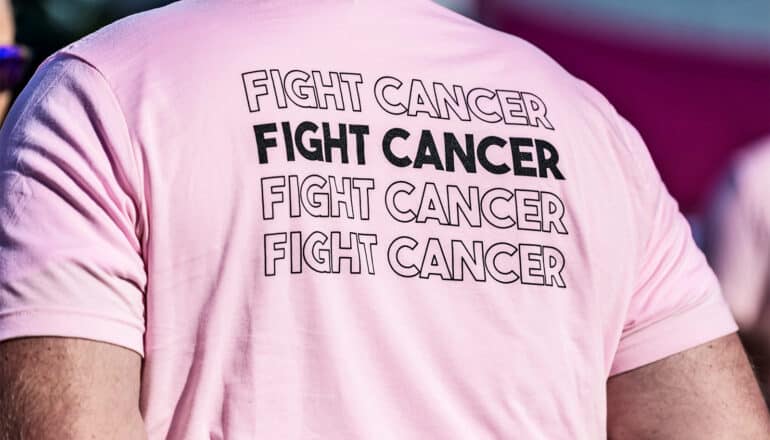A man wears a pink shirt with the words "Fight cancer" written four times on it.