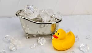 A yellow rubber duck toy next to a small silver bathtub replica filled with ice.