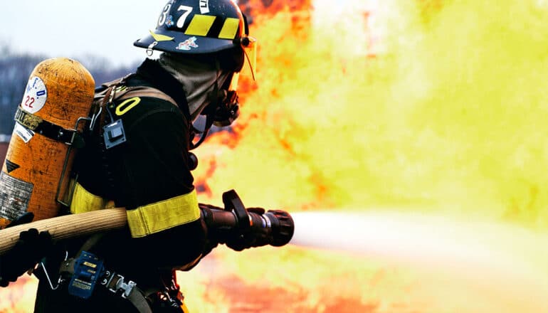A firefighter sprays water from a fire hose onto a fiery blaze.
