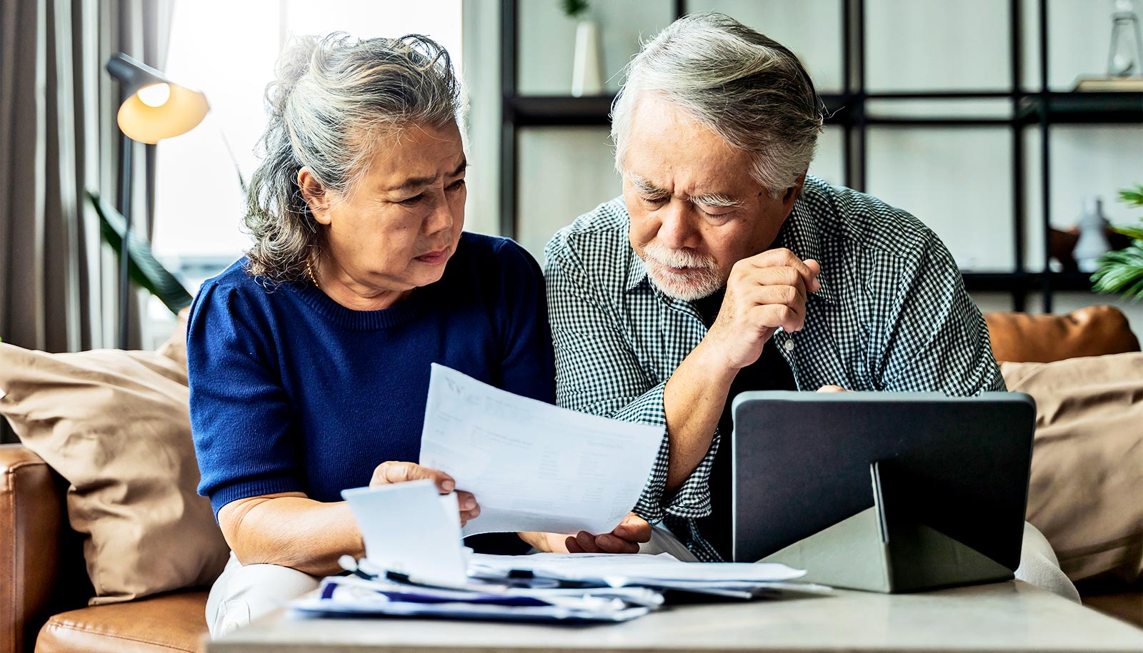 An older couple go over health care bills while sitting at a table together with a tablet computer.