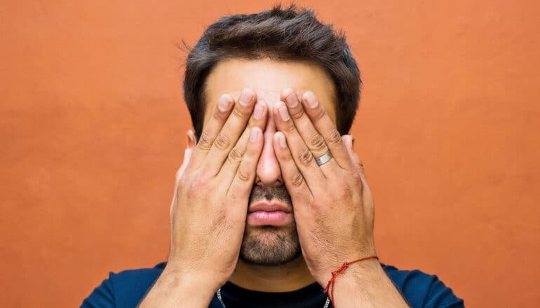 A man covers his eyes with both hands.