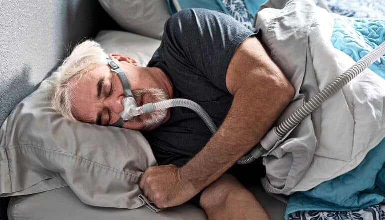 A man sleeps in bed while wearing a sleep apnea mask.