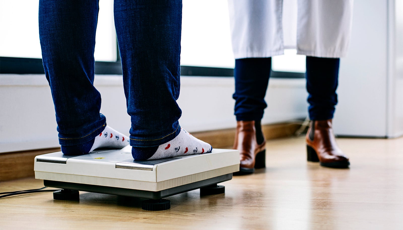 A patient's feet on a scale while the doctor stands nearby.