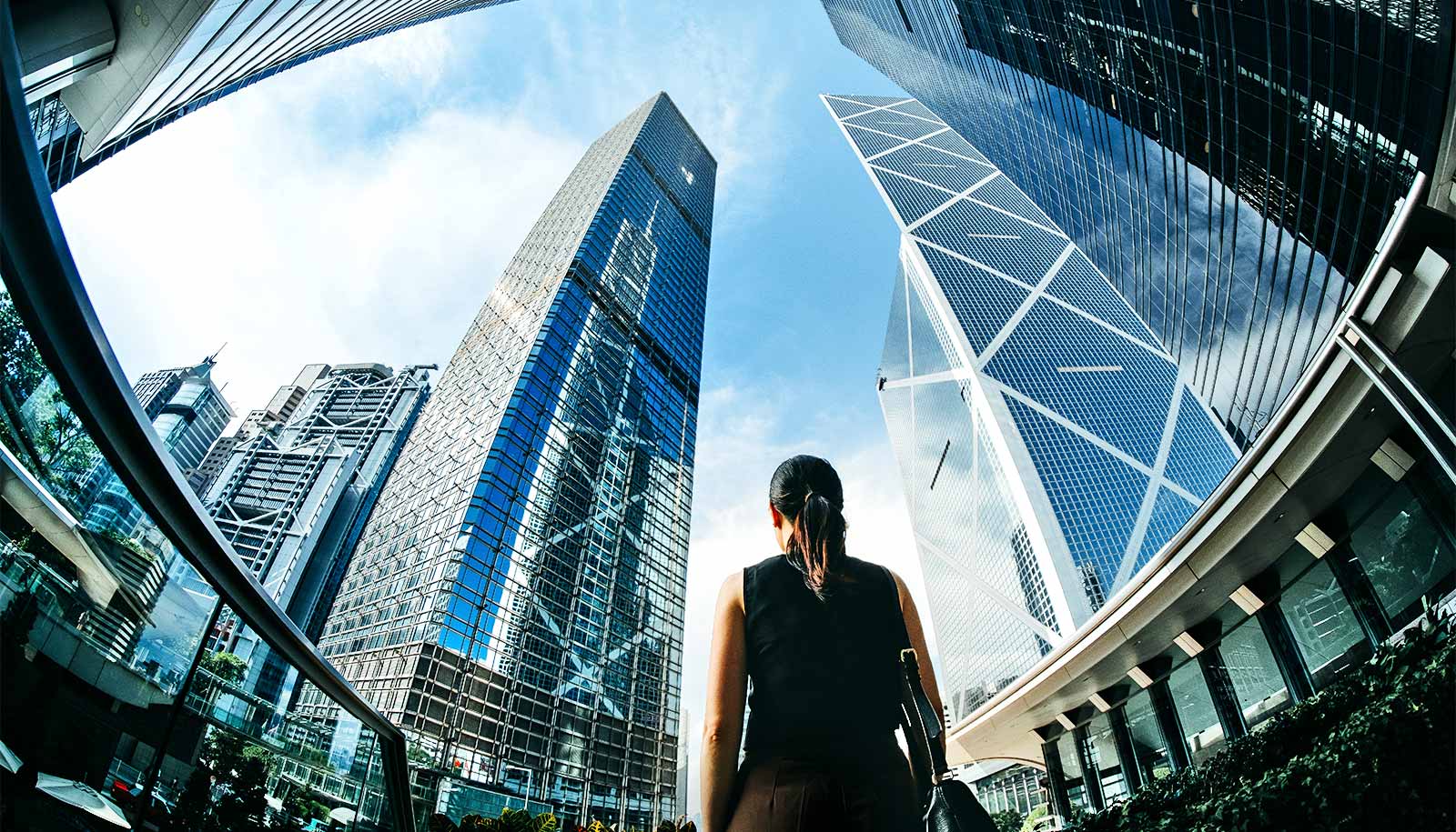 A woman walks through a city with large skyscrapers surrounding her.