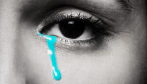 A tear highlighted in bright blue rolls down a woman's cheek.