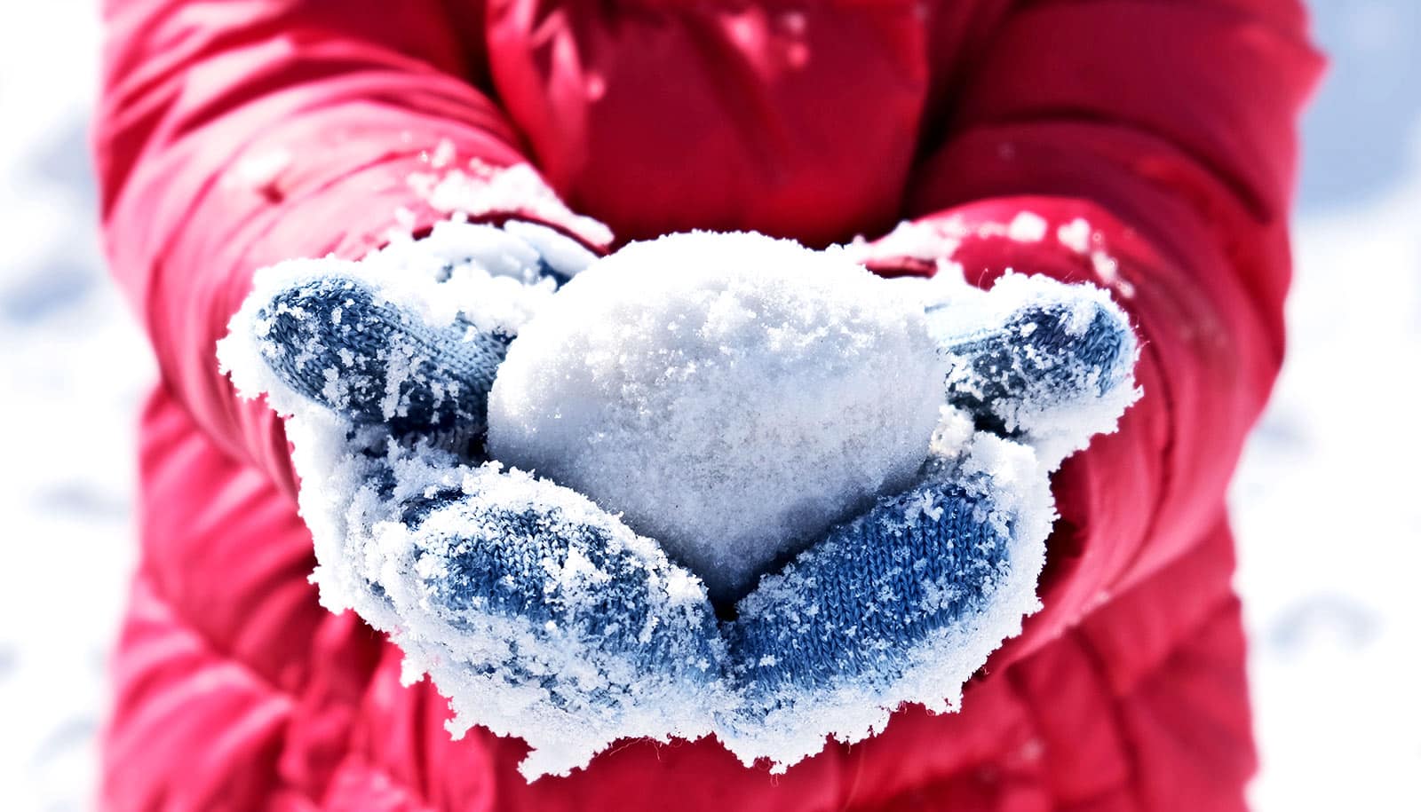 A child holds a snowball in gloved hands while standing outside in winter.