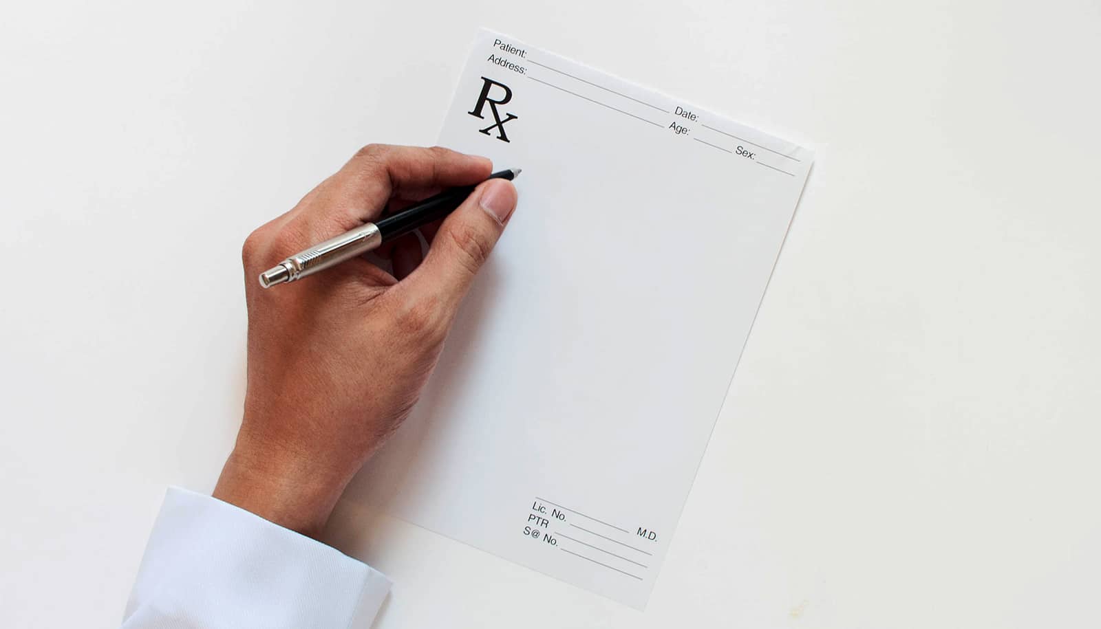 A doctor holds a pen over a blank prescription pad.