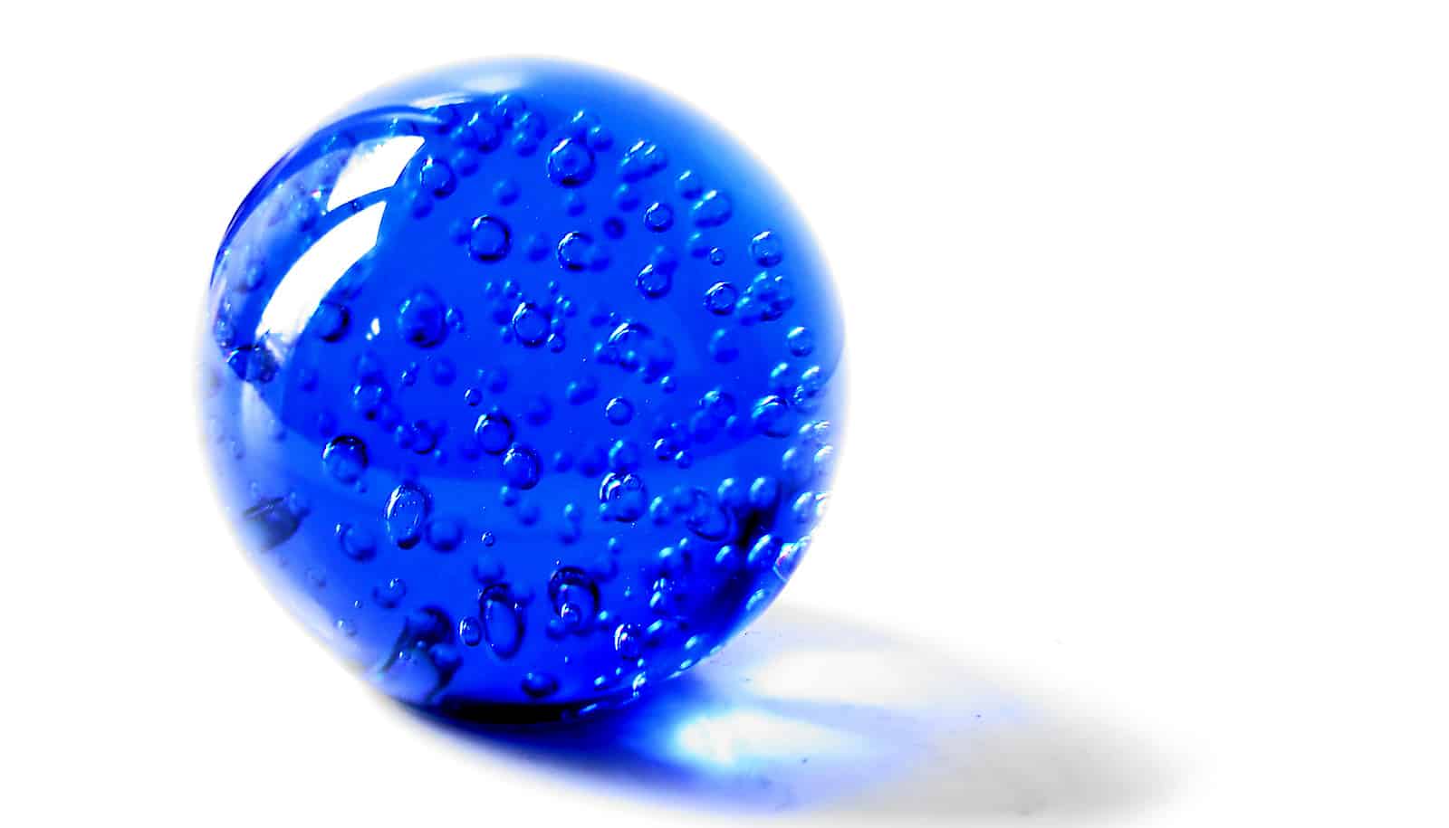 A blue marble with bubbles inside it sits on a white surface.