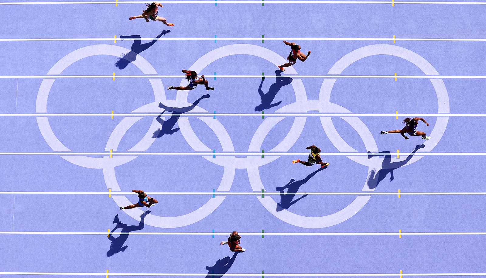 Runners race on a purple track with the Olympic ring logo on it.