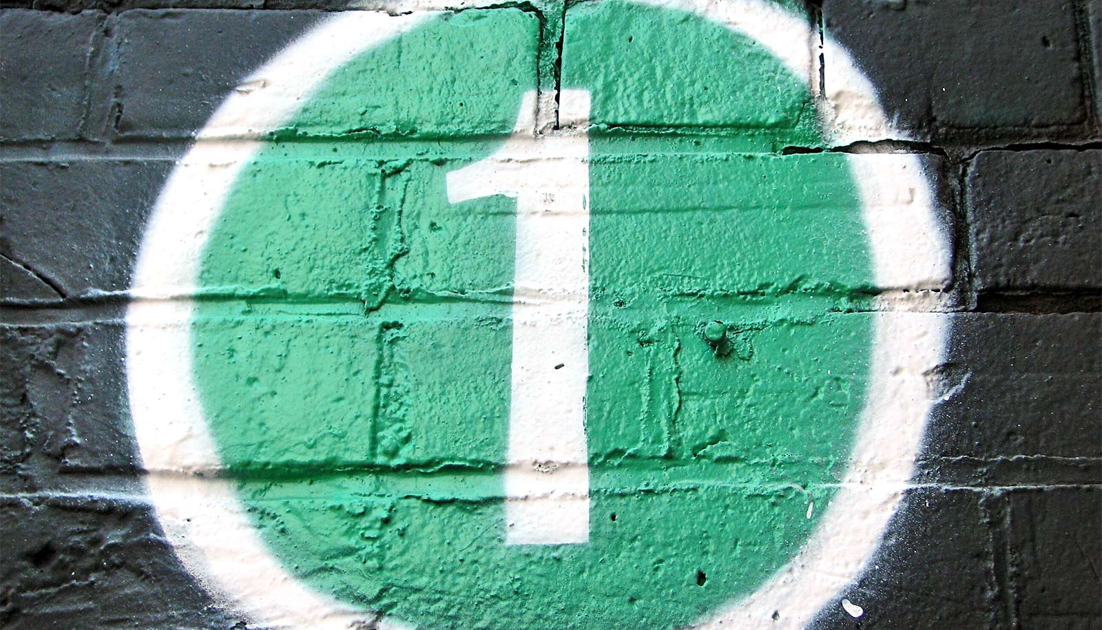 A number one painted in white inside a green circle on a black wall.