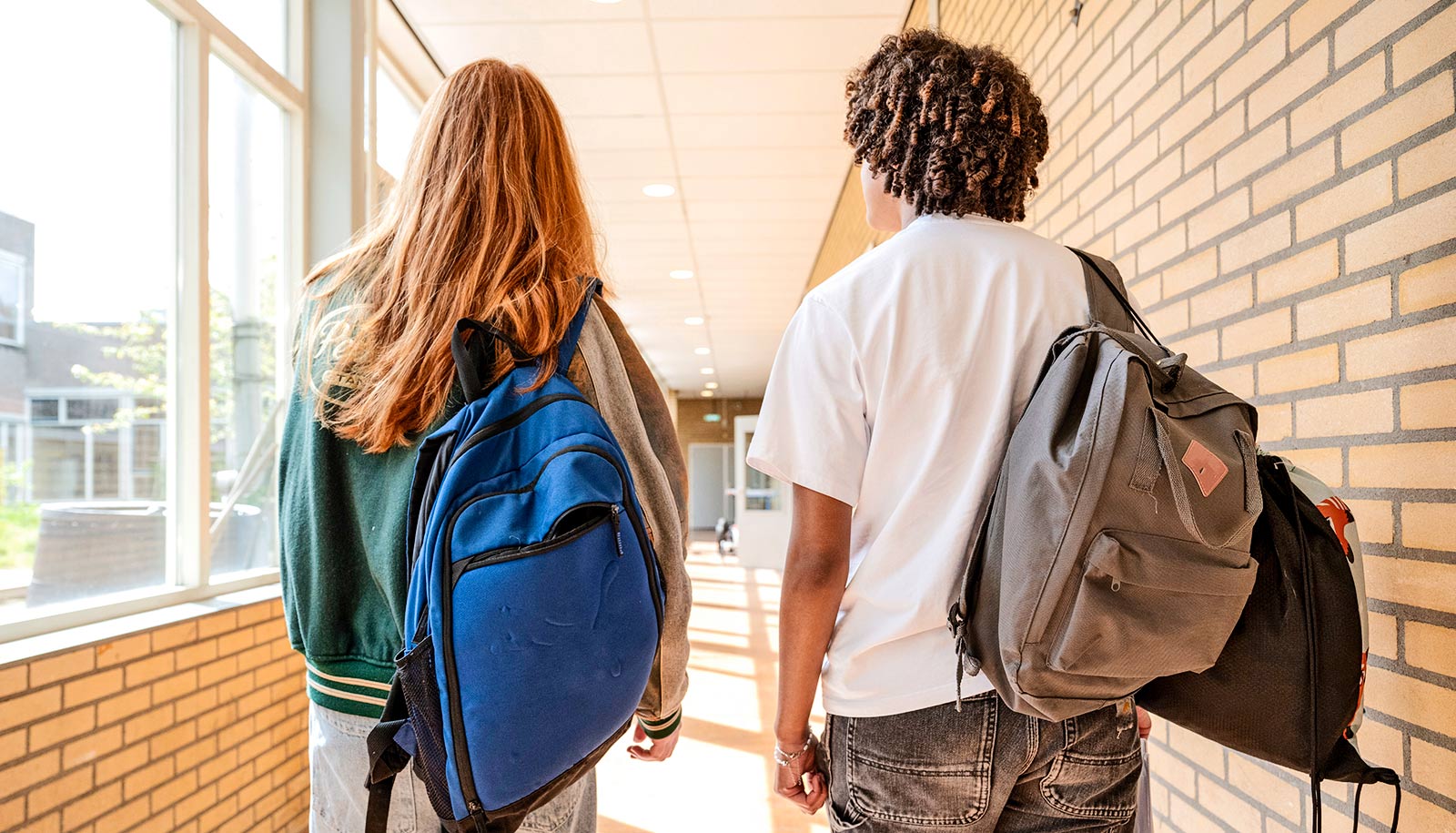Two high school students walk down a school hallway.