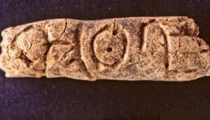 A small, brown clay cylinder with alphabetic writing carved into it.