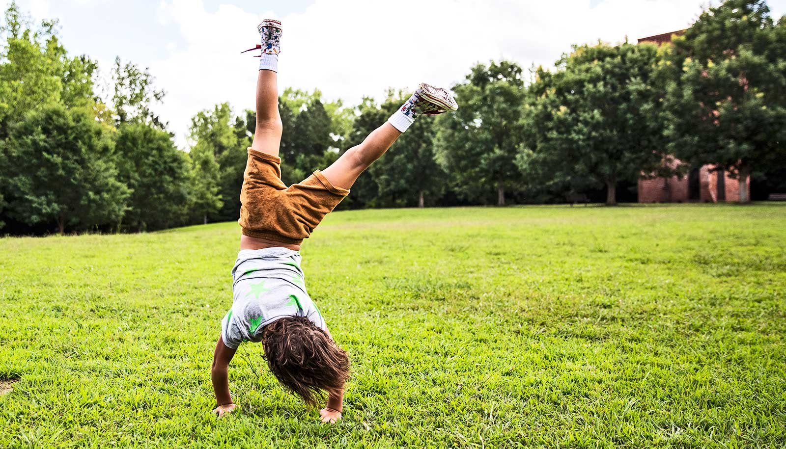 A young boy does a cartwheel in a field with trees in the background.