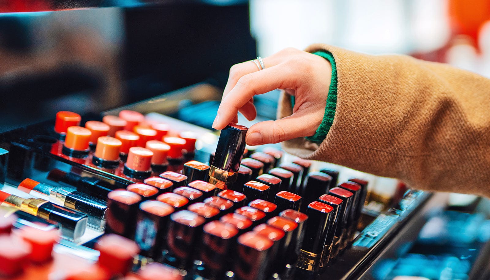 A young woman picks up a lipstick tube from a store display.