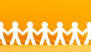 A chain of people cut out of white paper stands in front of a yellow background.