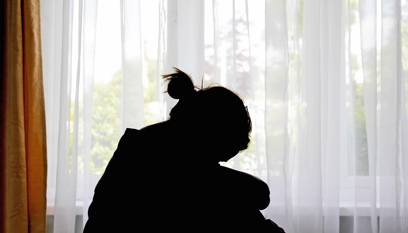 A woman's silhouette shows her huddled in profile in front of a window.